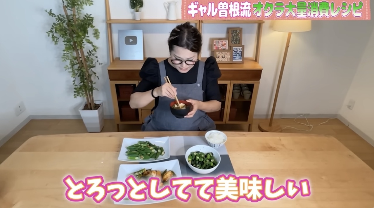 女性がテーブルで食べ物を食べています。背景にテレビと棚があります。テキスト：「ギャル曽根流 オクラ大量消費レシピ」「とろっとしてて美味しい」。