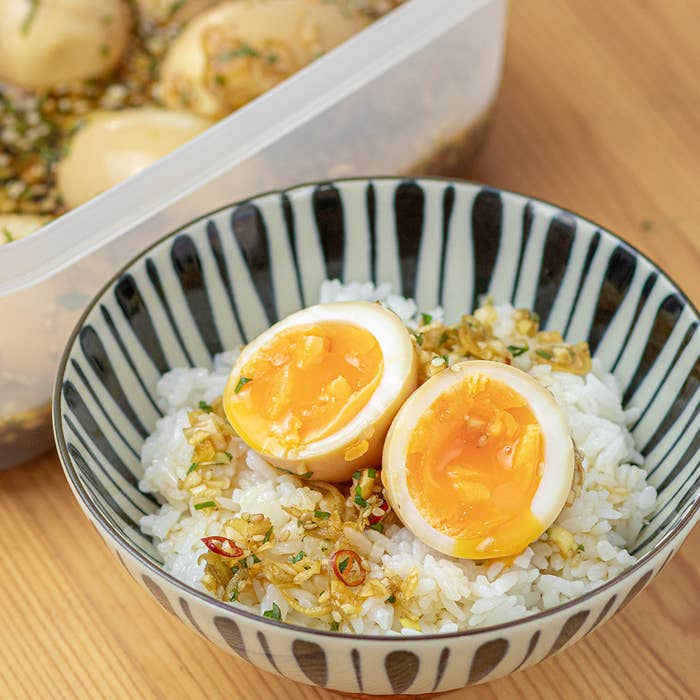 柔らかい煮卵が乗ったご飯のボウル、背景にタッパーに入った他の煮卵が見える。