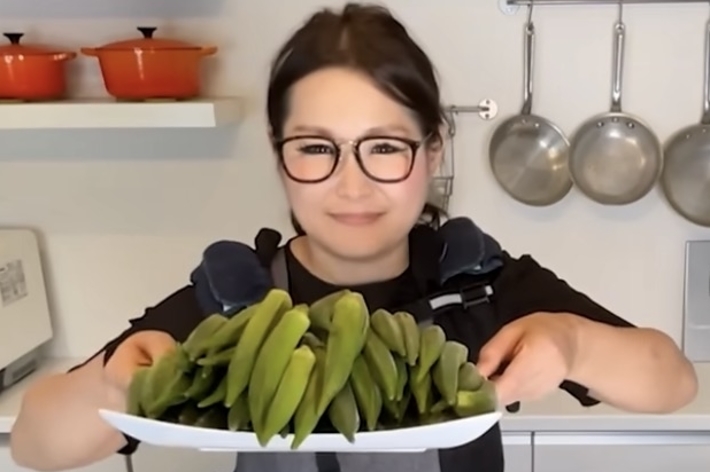 キッチンで若い女性がオクラを持って微笑んでいる。テキスト: 夏野菜 オクラ 第二弾