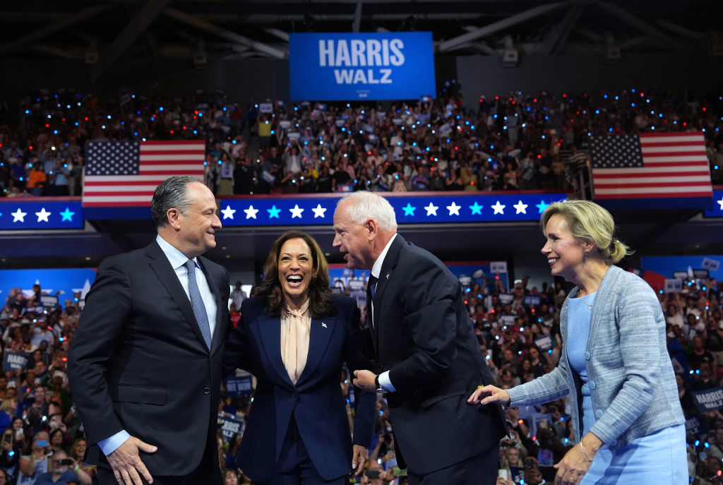 Doug Emhoff, Kamala Harris, Tim Walz, and his wife Gwen Walz smiling and interacting on stage at a rally