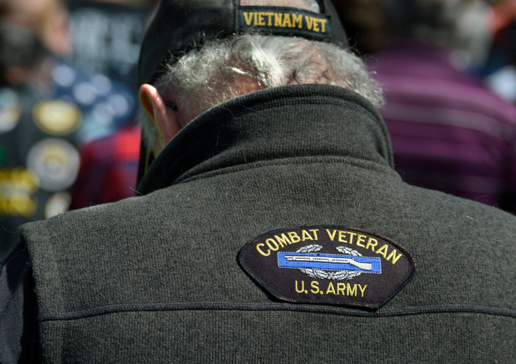 A person wearing a hat labeled &quot;Vietnam Vet&quot; and a jacket with a patch that reads &quot;Combat Veteran U.S. Army&quot; on their back