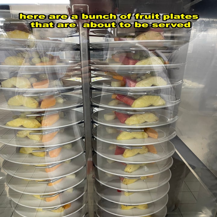 Several fruit plates stacked on a trolley, ready to be served. Text: "Here are a bunch of fruit plates that are about to be served."