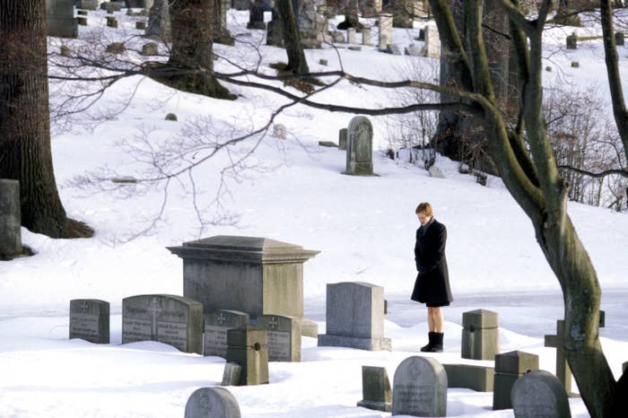 A person stands alone in a snow-covered cemetery, looking at the gravestones