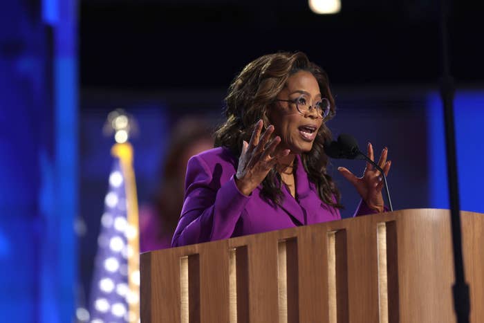 Oprah Winfrey speaks passionately at a podium during a public event, with an American flag in the background