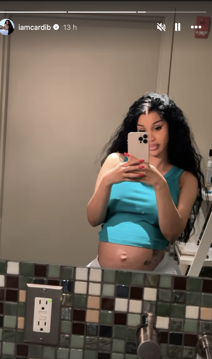 Cardi B takes a selfie in front of a bathroom mirror, showing her baby bump and wearing a sleeveless top