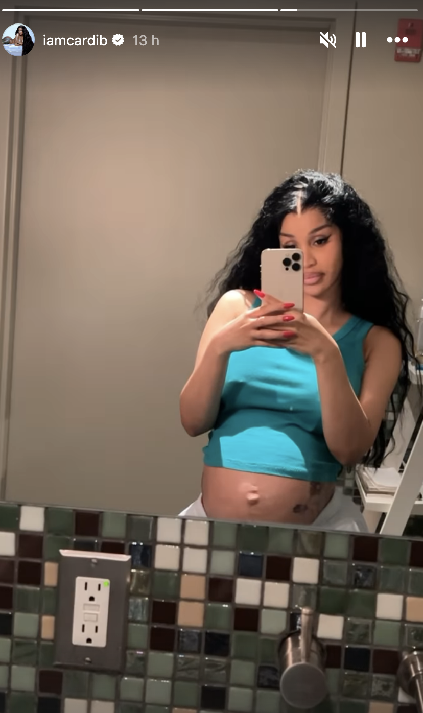 Cardi B takes a selfie in front of a bathroom mirror, showing her baby bump and wearing a sleeveless top