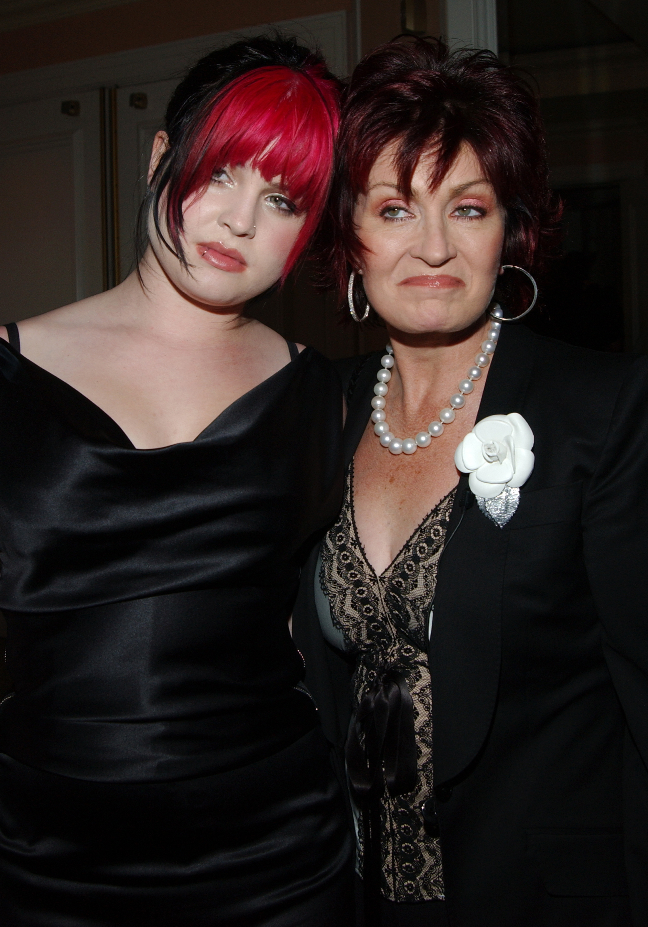 Kelly Osbourne in a dress standing next to Sharon Osbourne who&#x27;s in a dark blazer with a lace top and a rose brooch