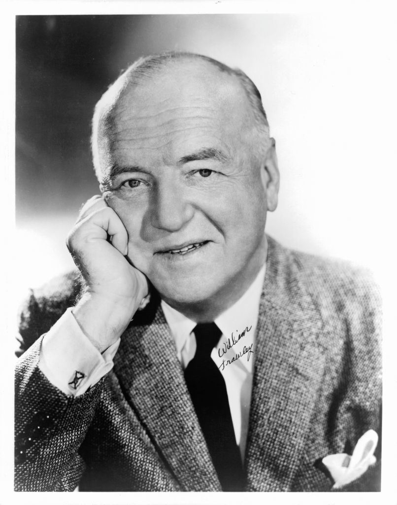 William Frawley in formal attire with a suit and tie, resting his head on his hand, smiling