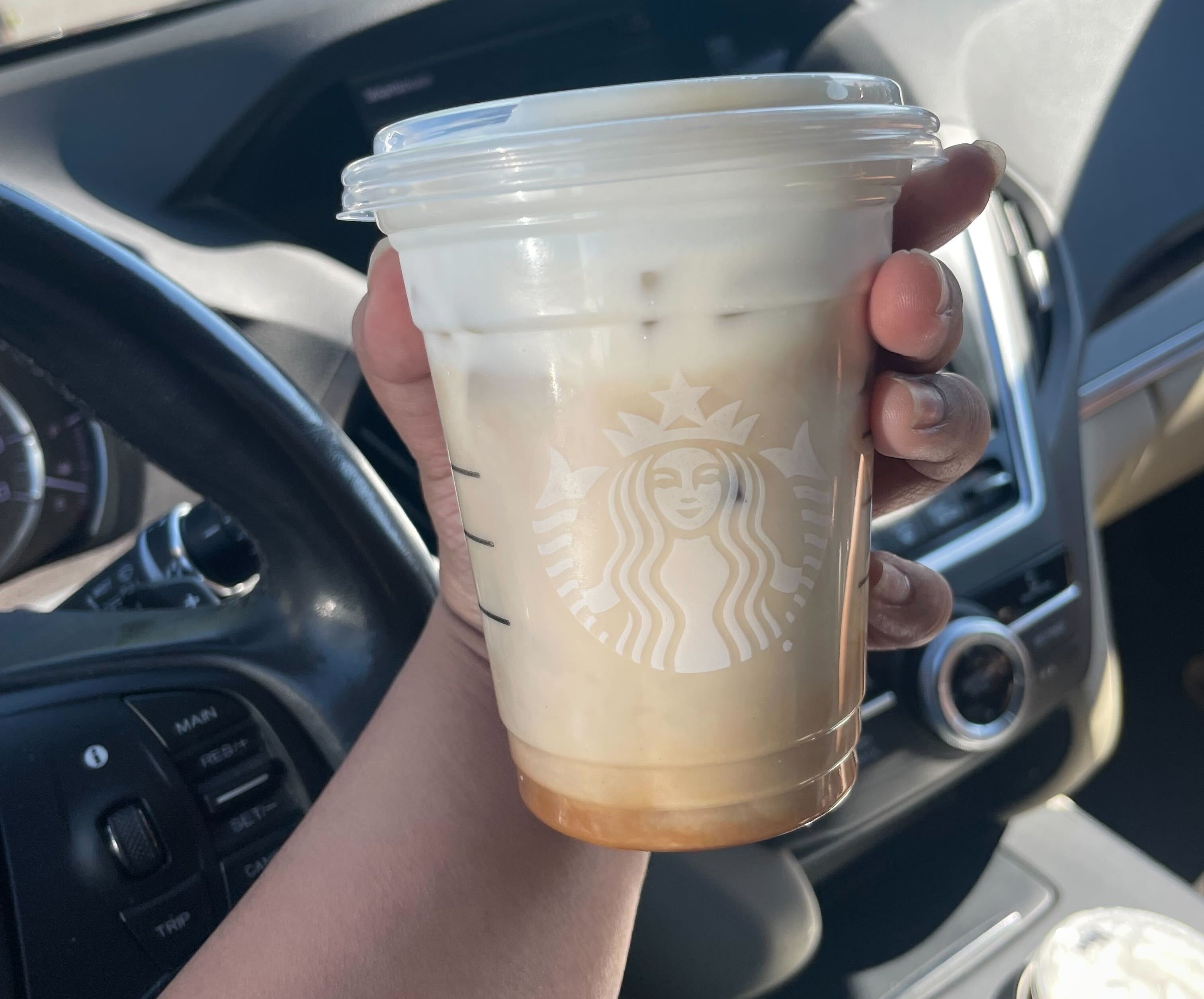 A hand holding a Starbucks drink in a car