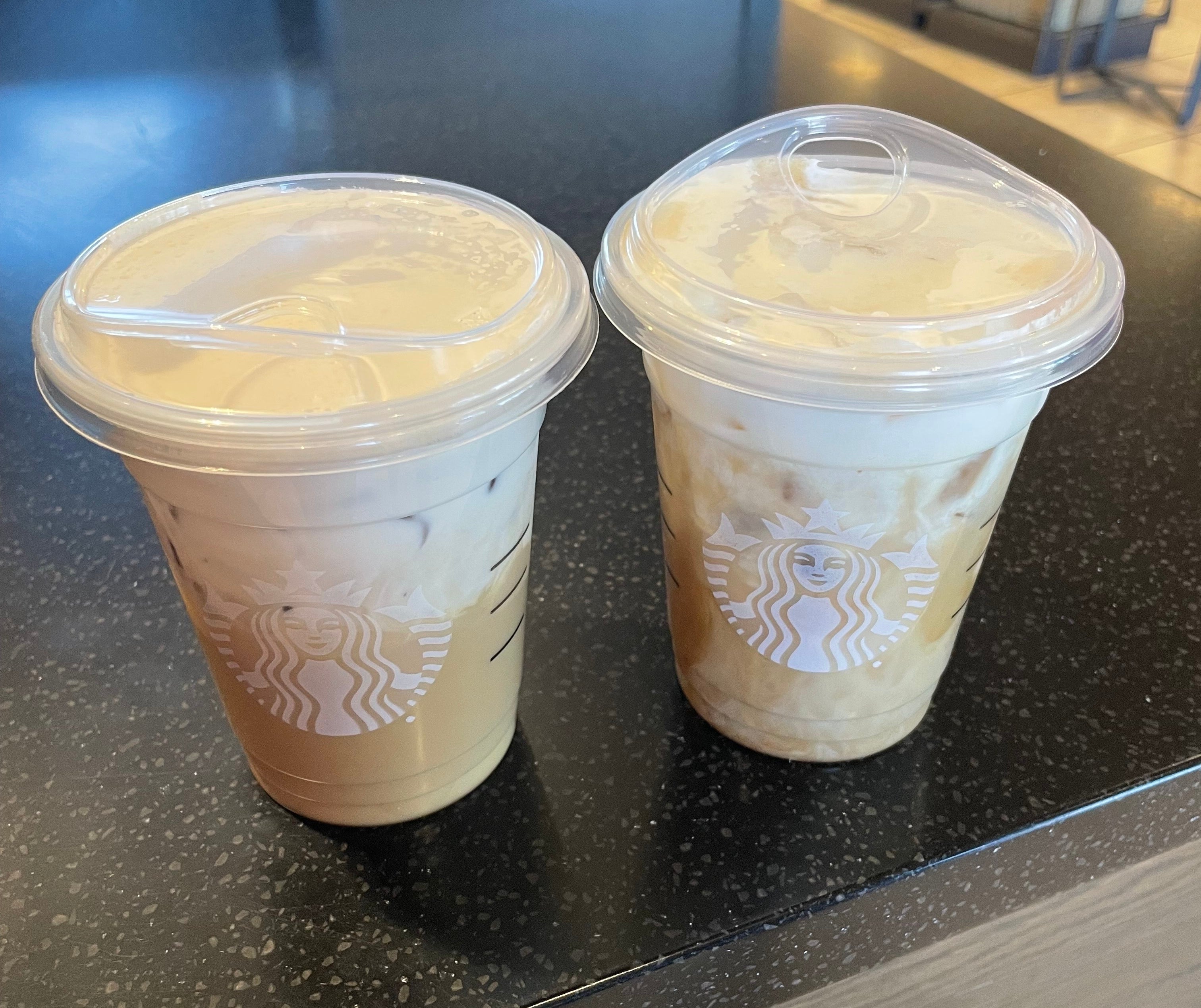 Two Starbucks cups, each with iced coffee topped with foam, placed on a dark counter in a coffee shop setting
