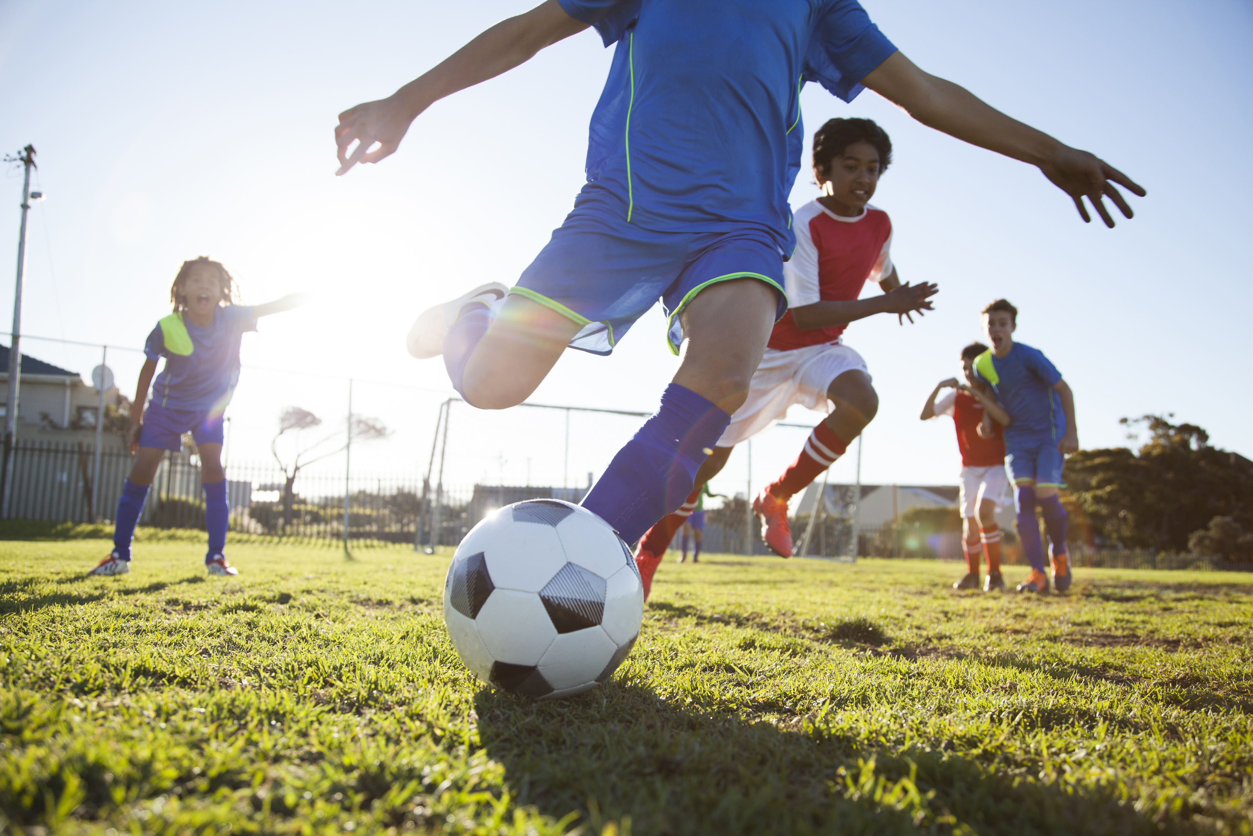 Children playing soccer on a grassy field, focusing on a child in blue kicking the ball while others run and play in the background