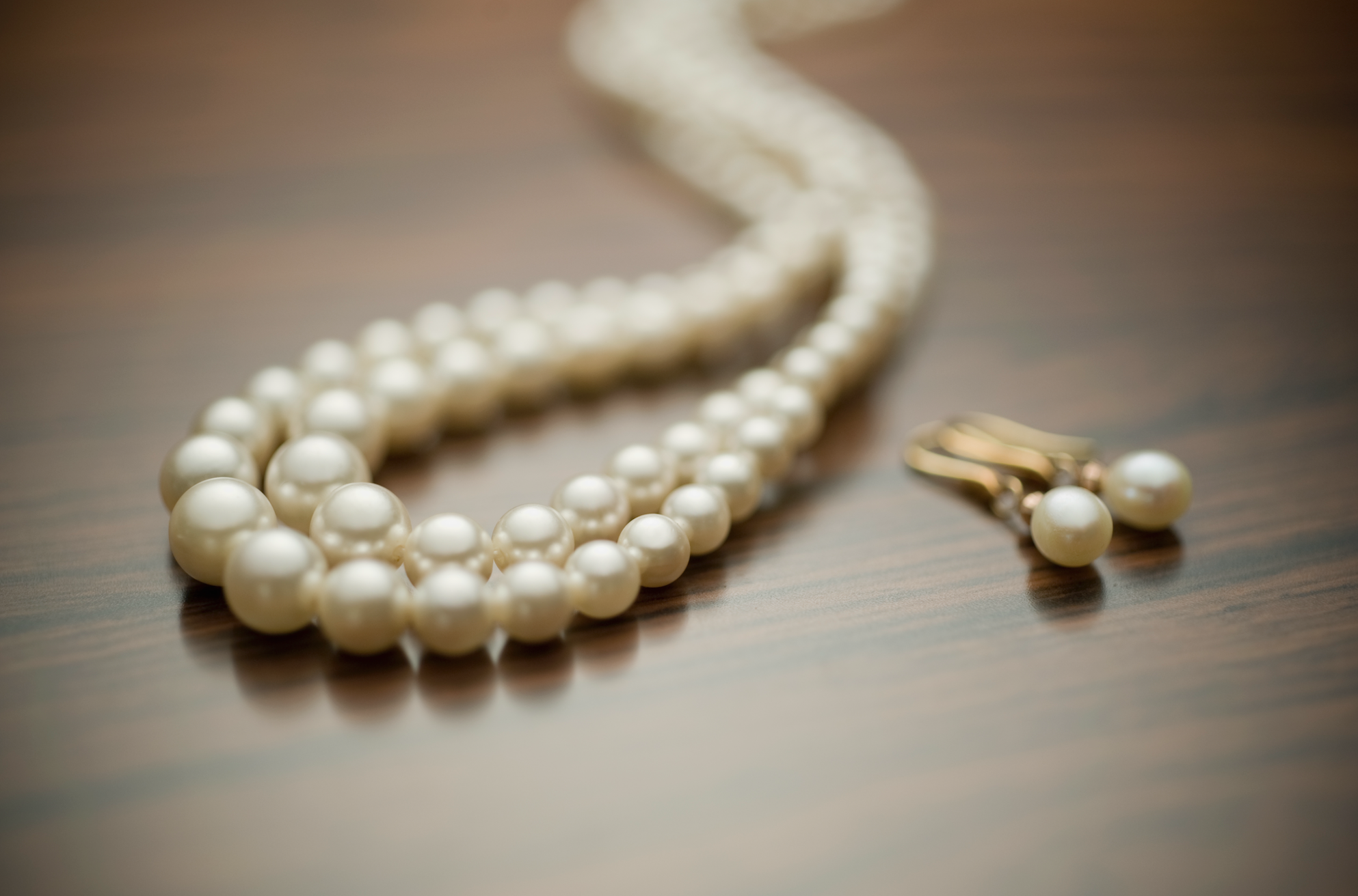 String of pearls and matching pearl earrings elegantly placed on a wooden surface. No persons in the image