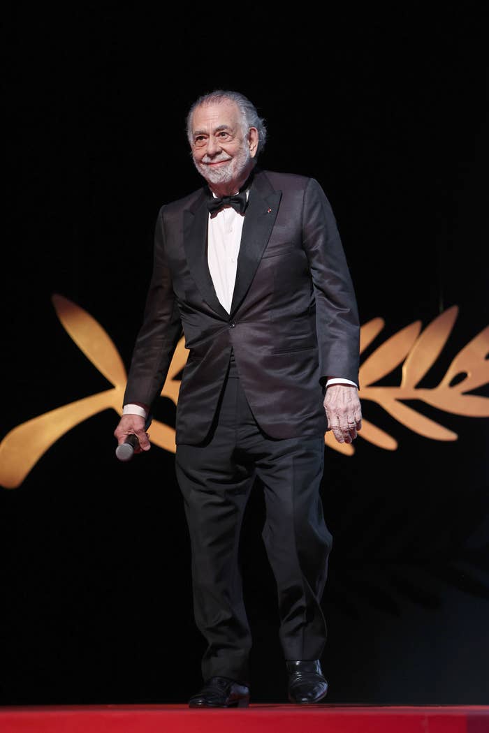 Francis Ford Coppola stands on stage in a tuxedo holding a microphone at a film festival event