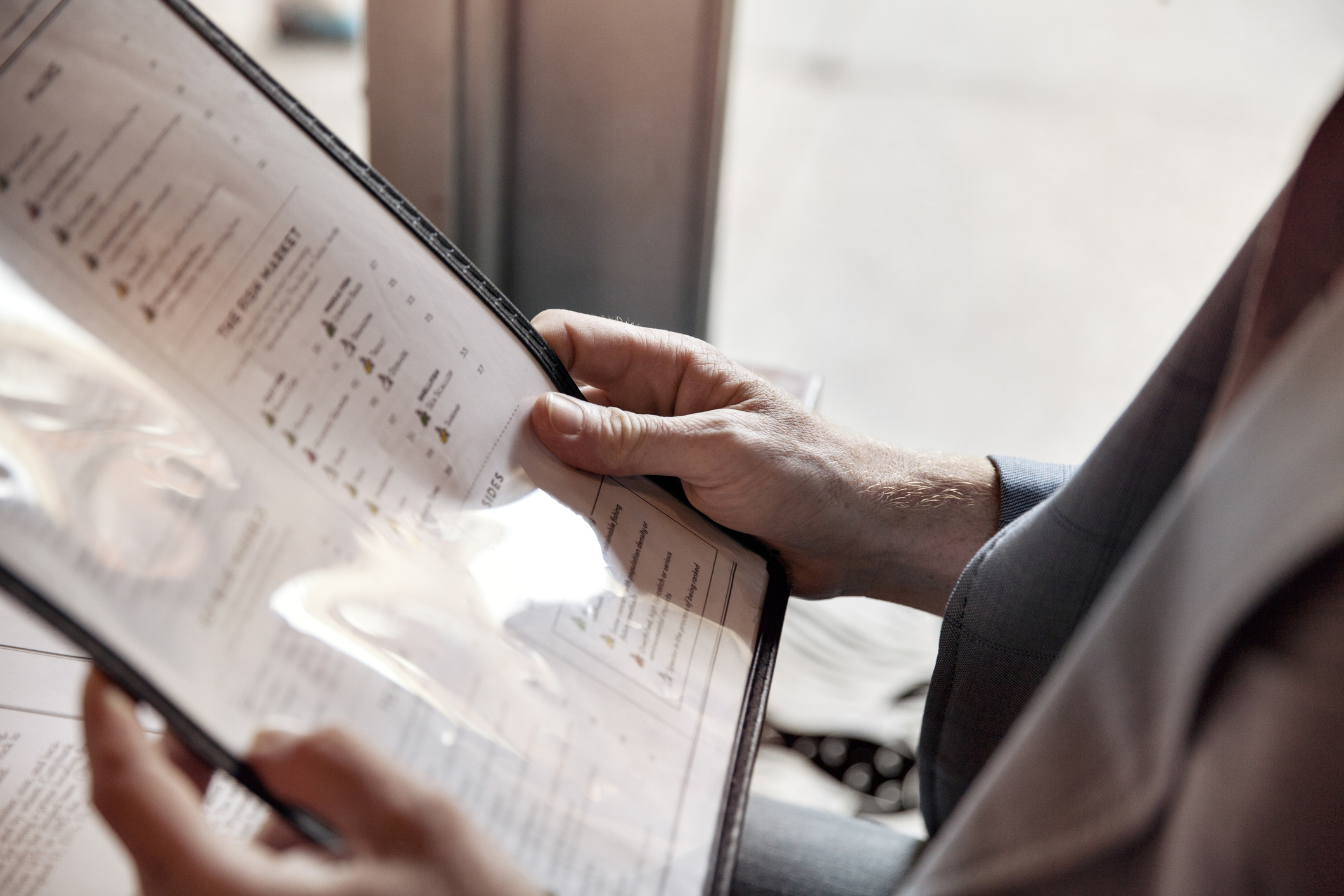 A person is holding a laminated menu, reading the food and drink options inside a restaurant. Their face is not visible
