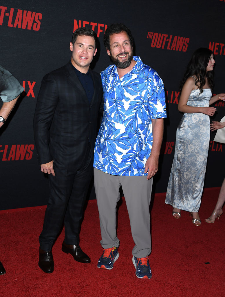 Adam Devine in a suit and Adam Sandler in a casual shirt and sneakers on the red carpet at The Out-Laws premiere