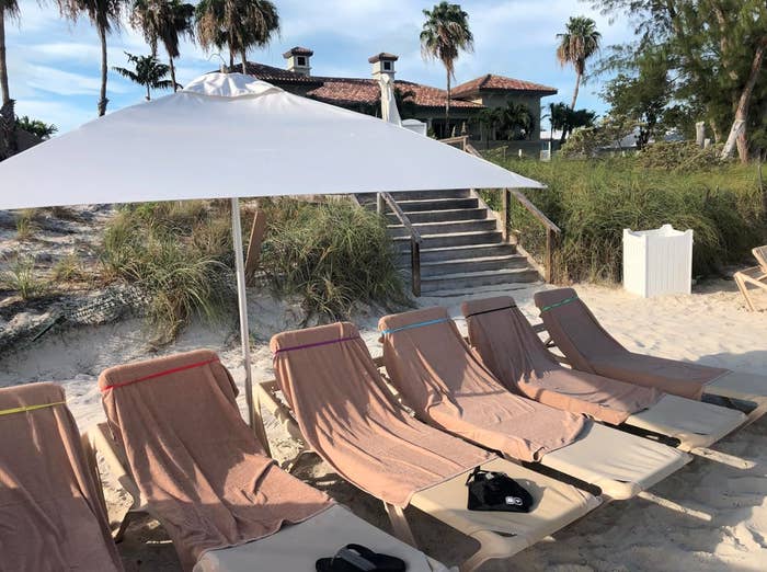 A formation country with six bare lounge chairs nether a achromatic umbrella, with a formation location and thenar trees successful the background