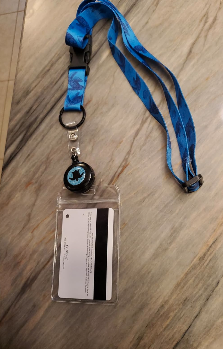 A blue lanyard with a retractable clip, a clear plastic ID holder, and a white card is displayed on a stone surface