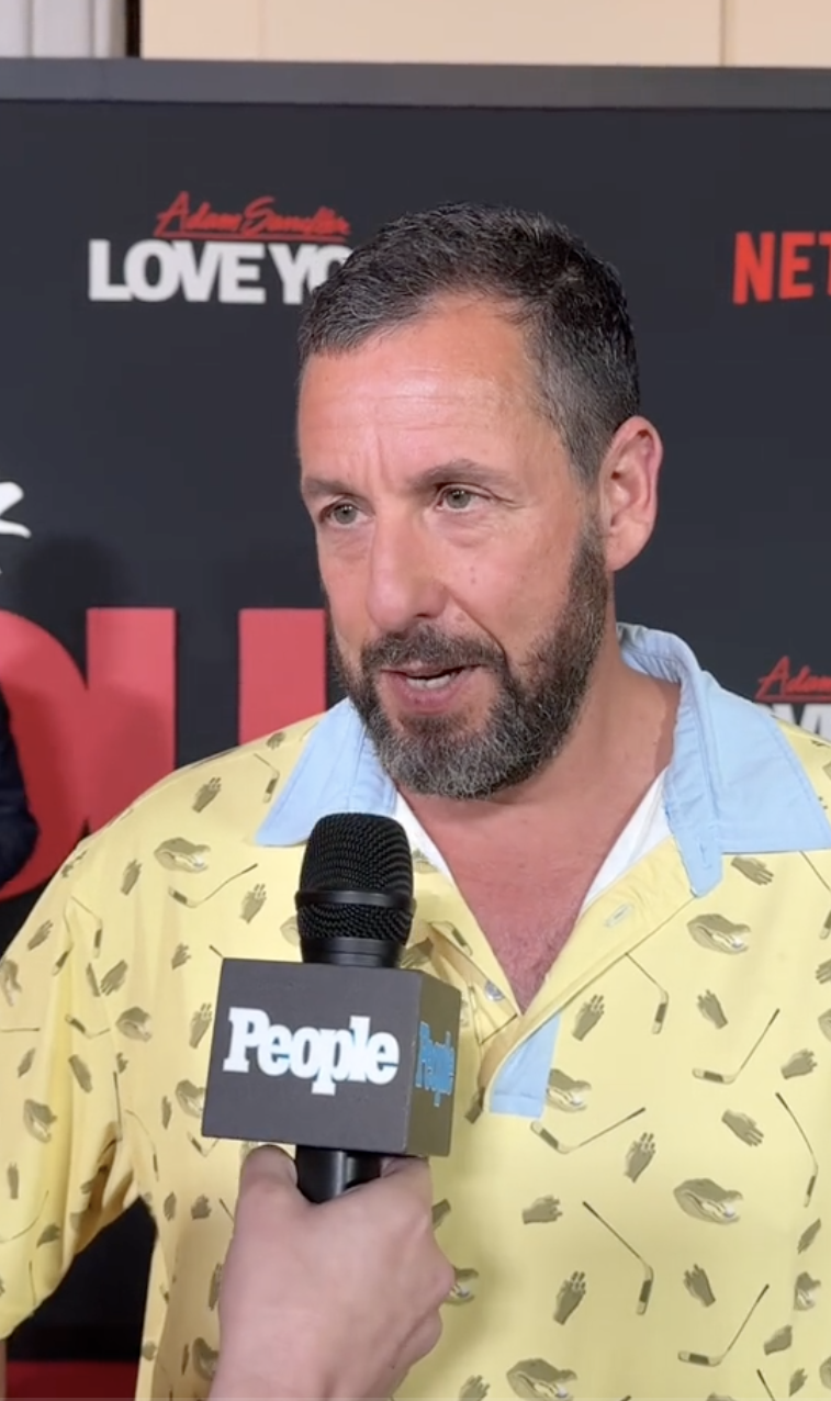 Adam Sandler being interviewed on the red carpet, wearing a casual shirt with a unique pattern, at the premiere of a Netflix project