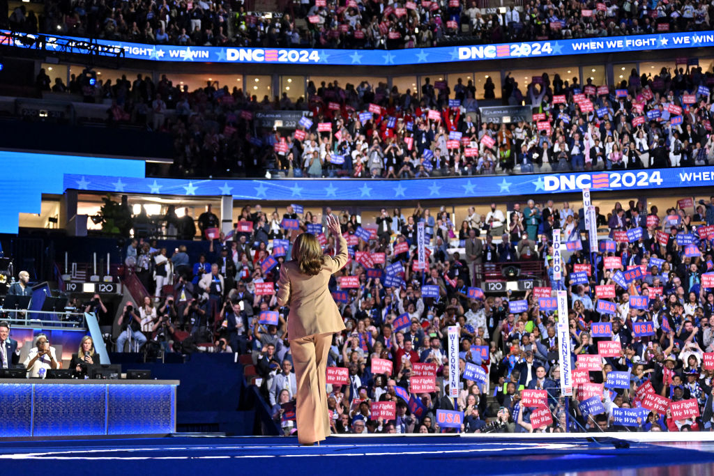 Kamala Harris on stage at DNC 2024 with a crowd holding signs