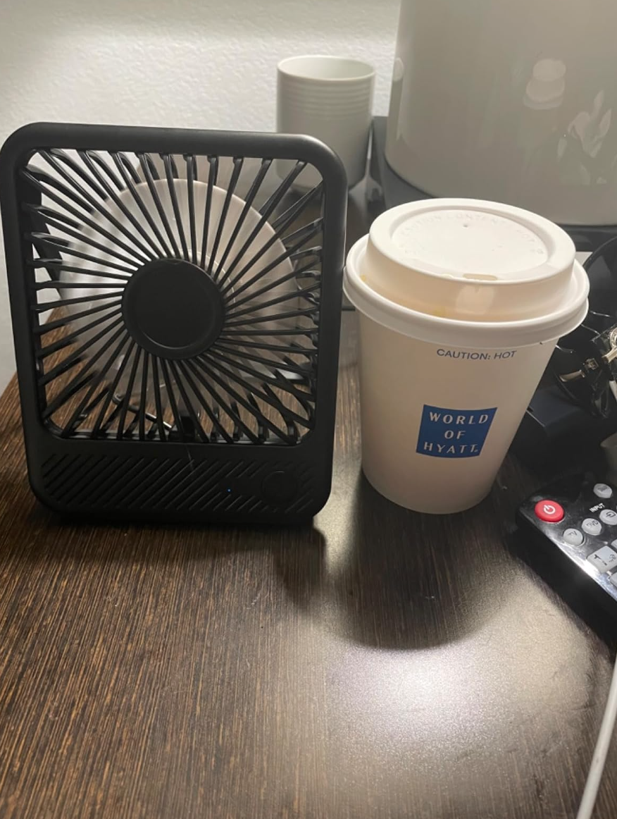 Table with a small desk fan and a coffee cup labeled "World of Hyatt."