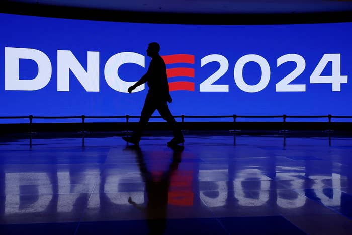 A person walks in silhouette against a large blue screen displaying the text &quot;DNC 2024.&quot;