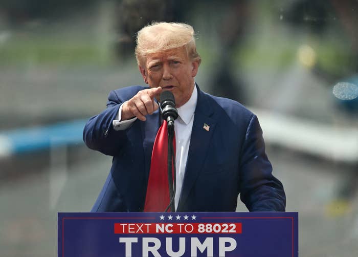 Donald Trump speaks at a podium with a "Text NC to 88022 Trump" sign, pointing towards the audience
