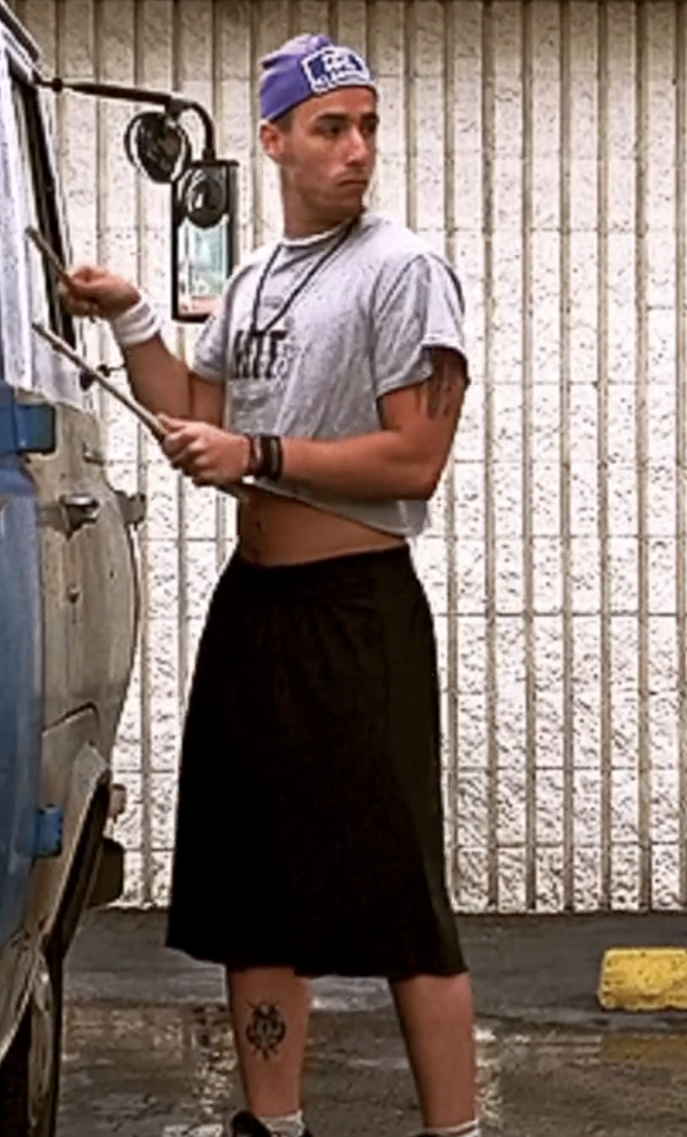 Adam dressed in casual sportswear, including a cropped T-shirt, long shorts, a baseball cap, wristbands, and sneakers