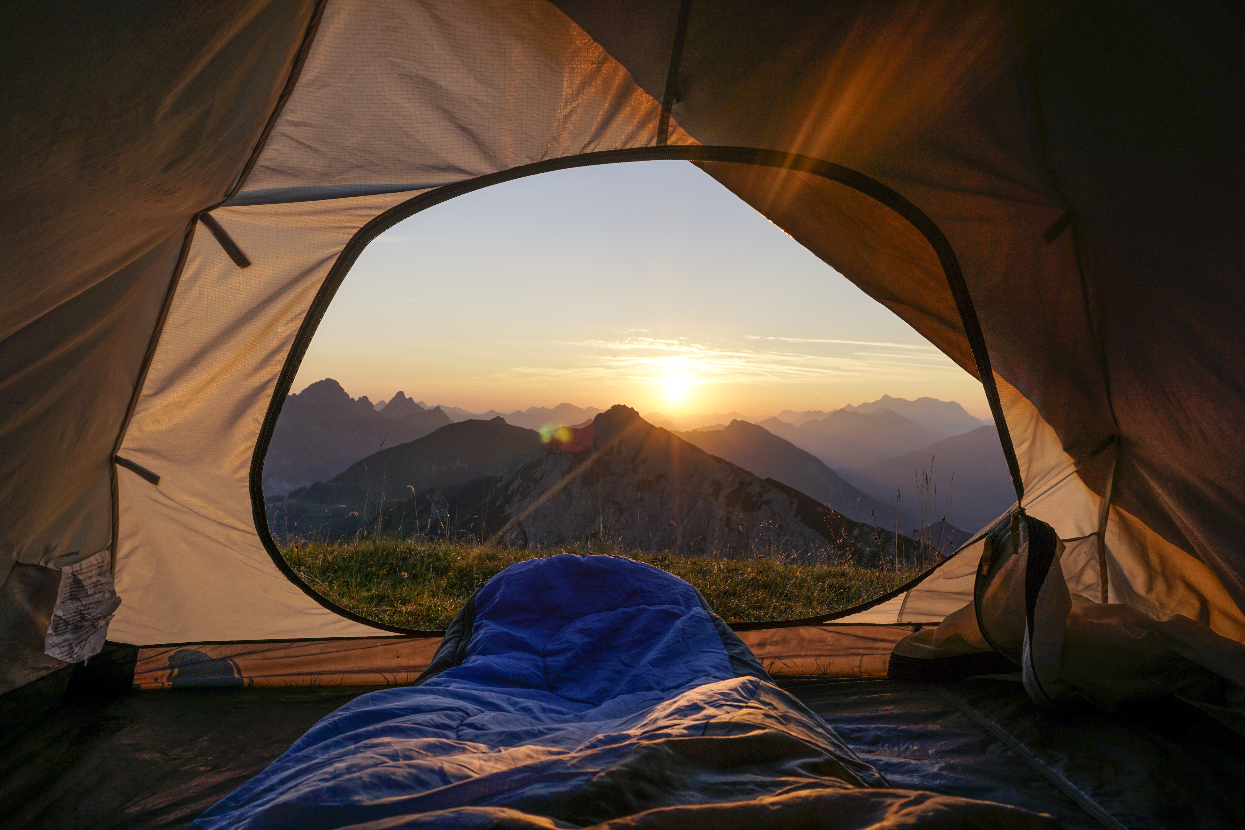 View from inside a tent looking out at mountains during sunrise with a sleeping bag in the middle