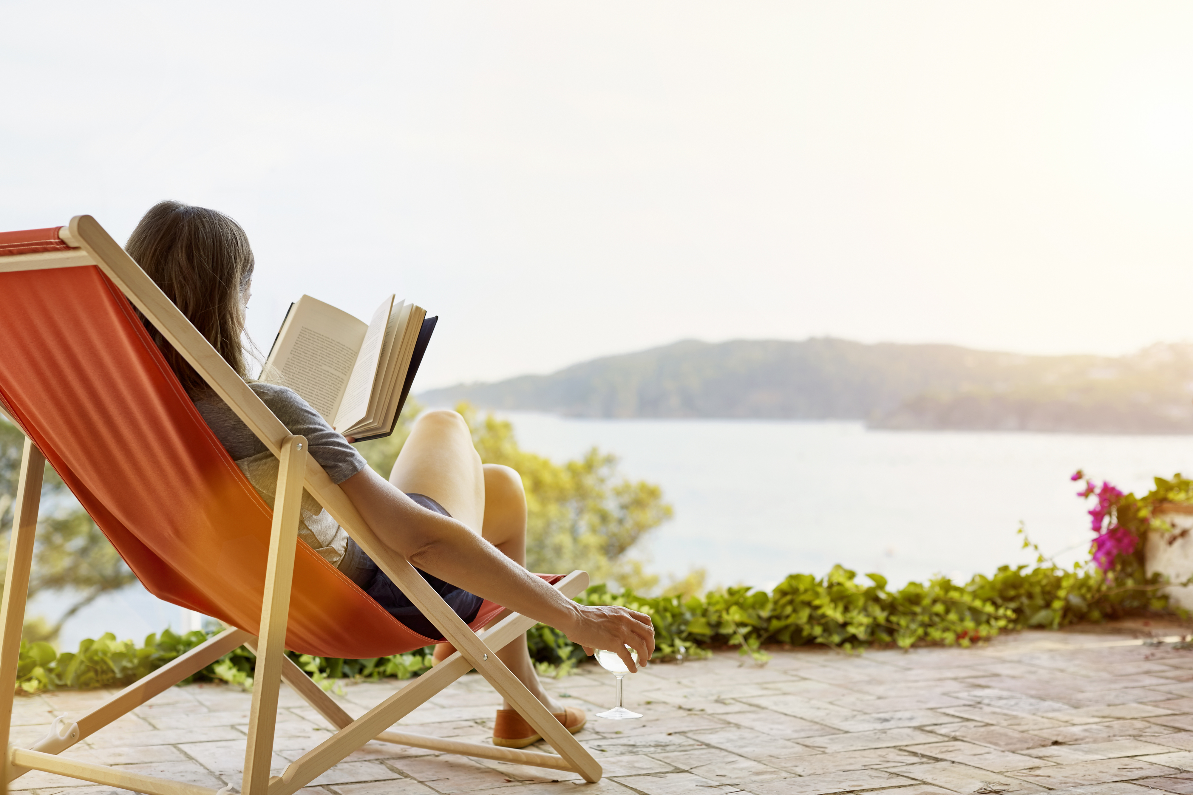 Person reading a book on a lounge chair with a waterfront view