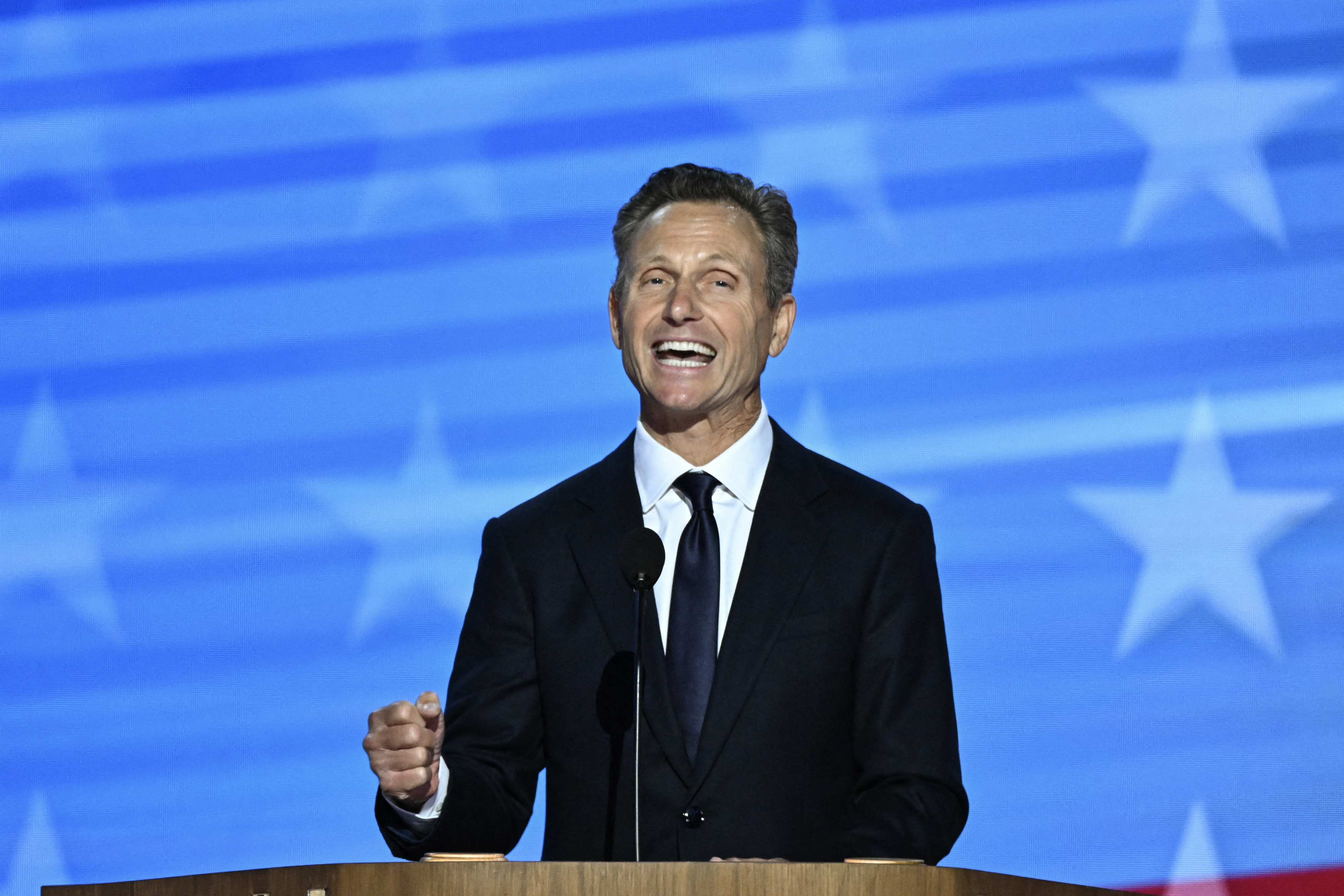 A man in a suit and tie is speaking at a podium with an American flag-themed background