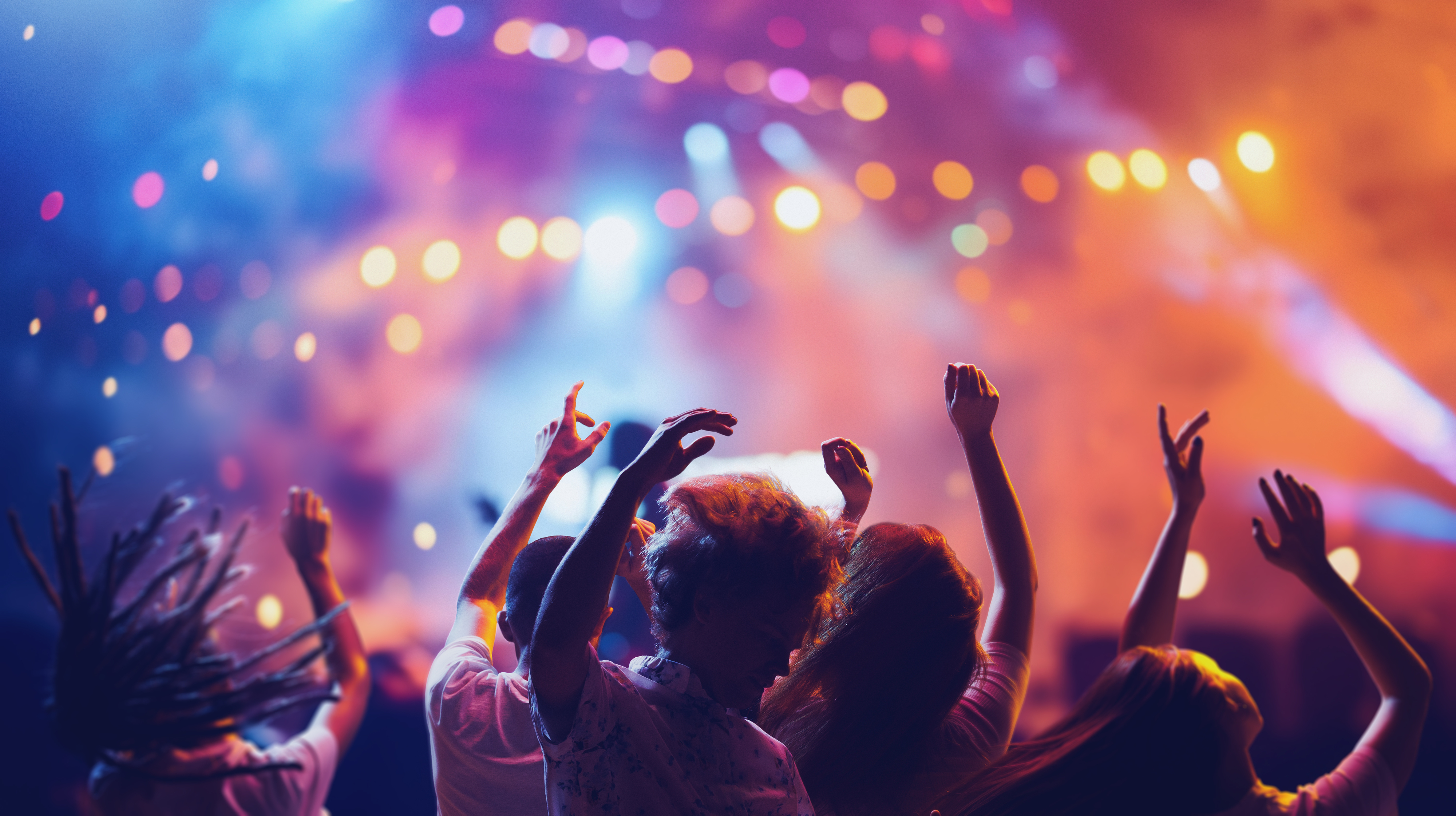 People enjoying a lively outdoor concert at night with vibrant lights illuminating the stage