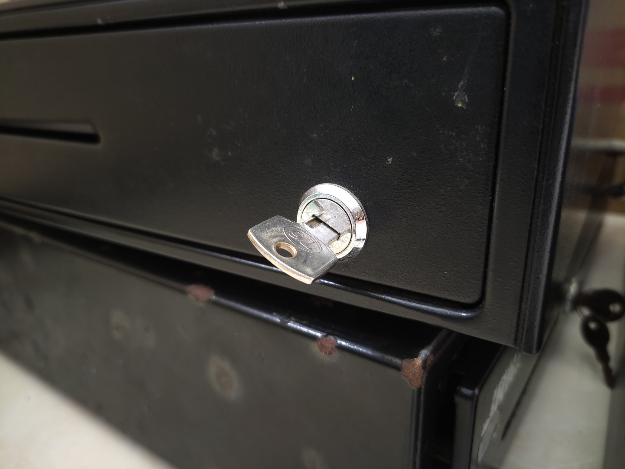 Close-up of a key inserted into the lock of a black drawer or cash register