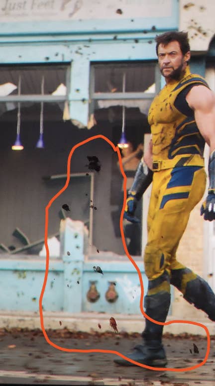 Hugh Jackman in Wolverine costume walking past a damaged building, with an edited orange oval highlighting around him. Debris is scattered in the scene