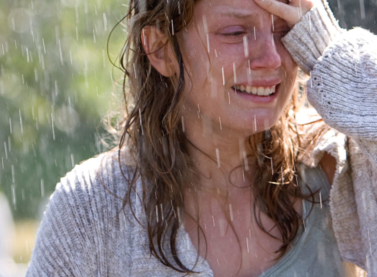 Woman smiling and holding her forehead, standing in the rain with a picket fence in the background