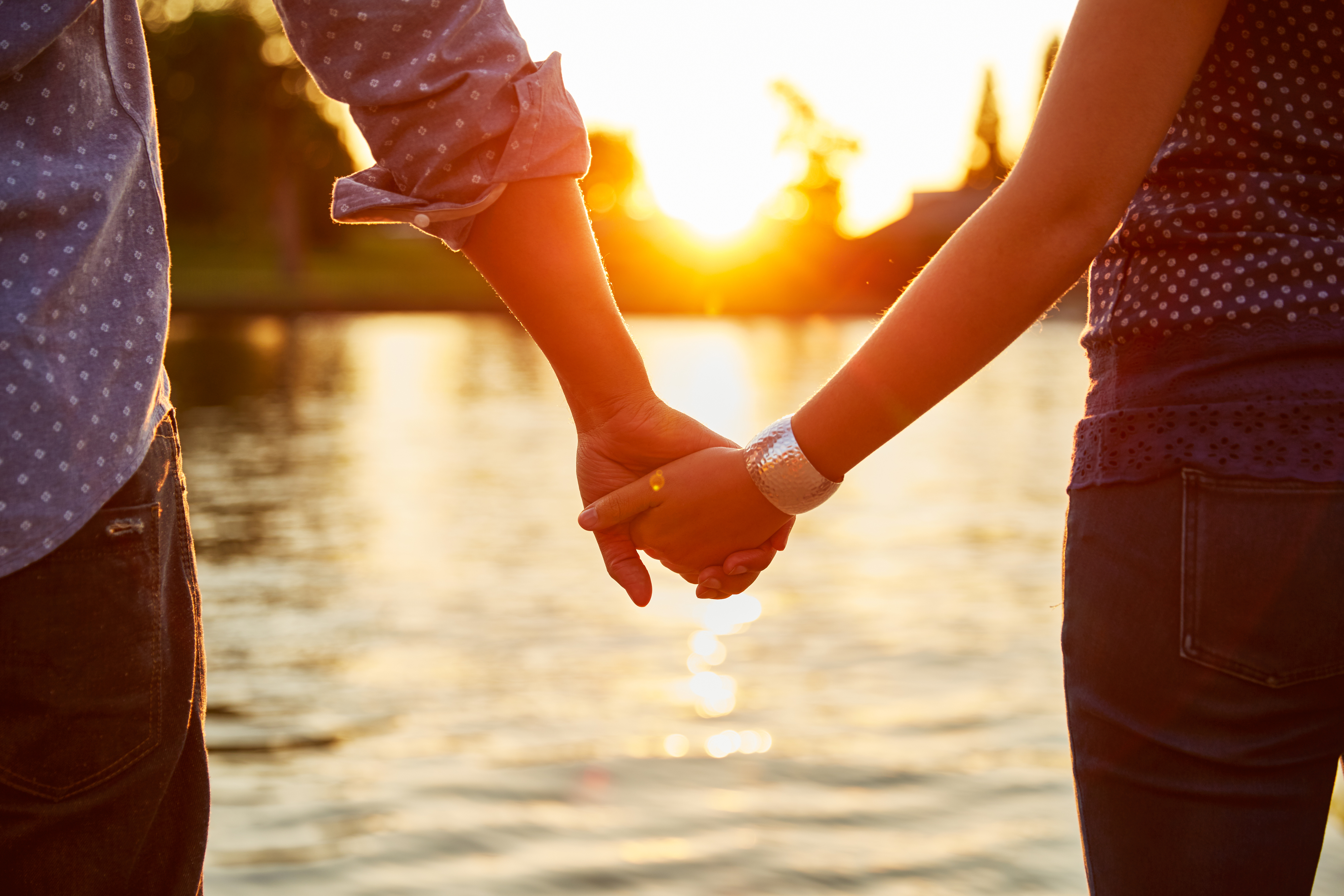 A couple holding hands near a body of water at sunset