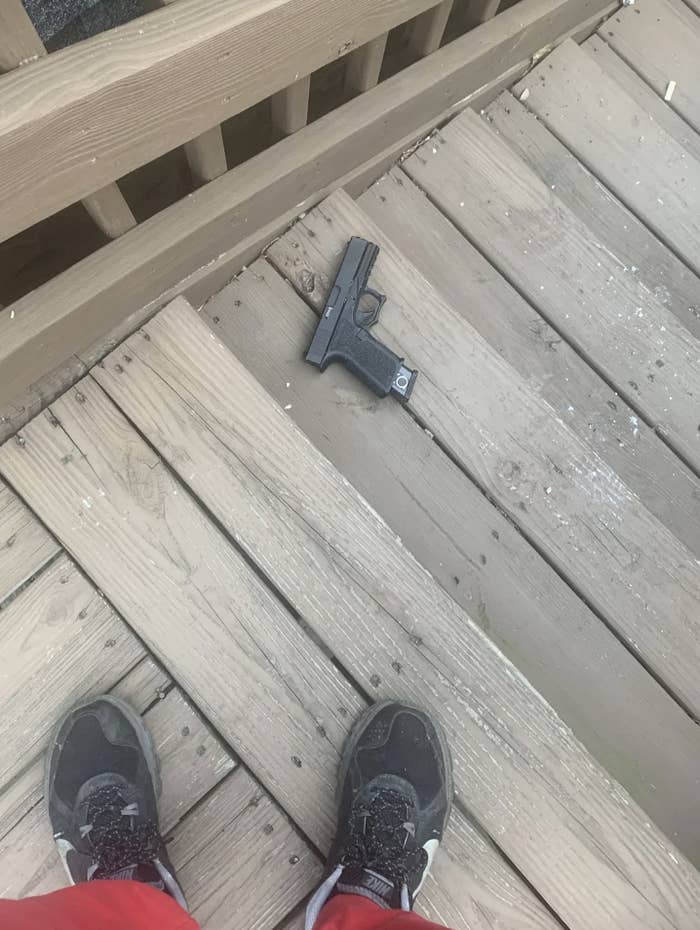 A pair of feet in sneakers standing on a wooden deck with an object resembling a pistol lying on the ground