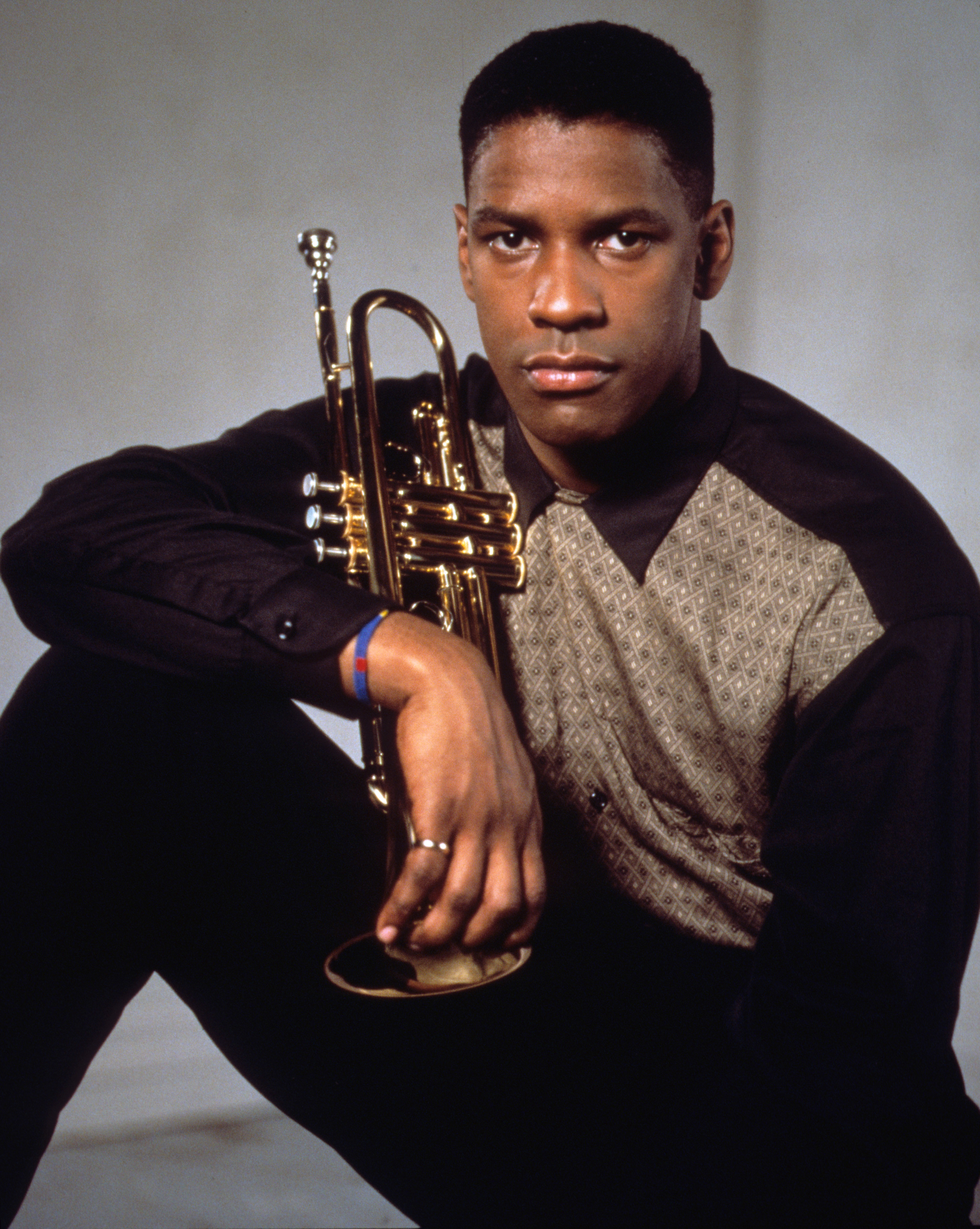 Denzel Washington, dressed in a patterned shirt, holds a trumpet