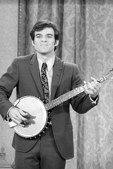 celeb plays the banjo while wearing a suit and tie