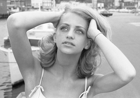 Young woman looking up with hands placed behind her head, standing near a waterfront