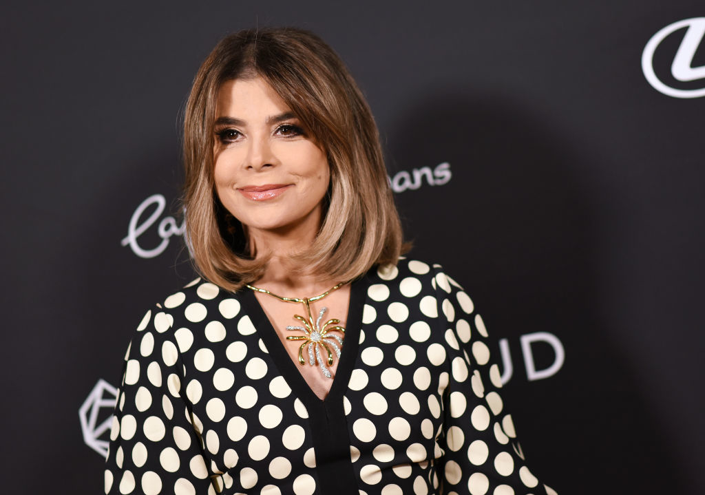 Paula Abdul on the red carpet in a polka dot dress with a deep V-neck and a gold necklace with a large pendant