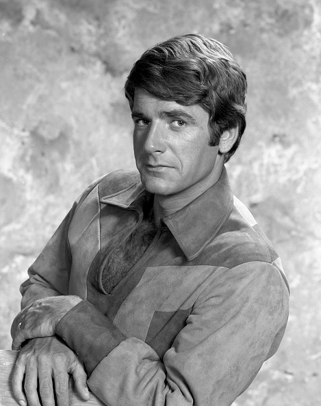 A person poses for a portrait in a vintage-style outfit with a serious expression