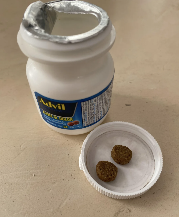 An Advil bottle with its cap off reveals two brown tablets inside the lid