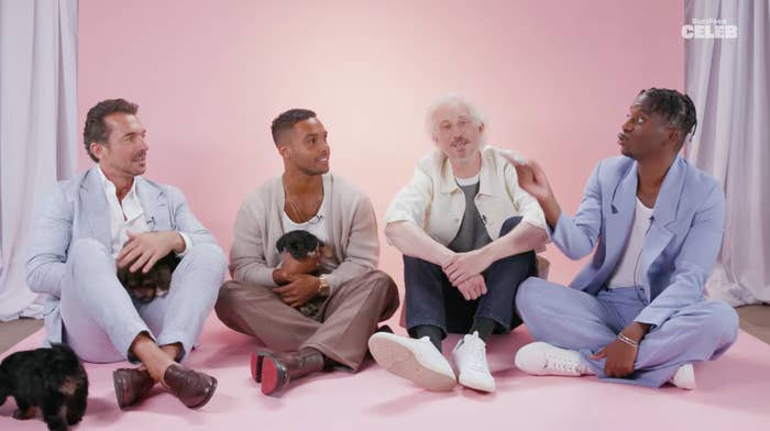 Lucien Laviscount, Bruno Gouery, Samuel Arnold, and William Abadie sitting on the floor with puppies, having a casual conversation against a light backdrop