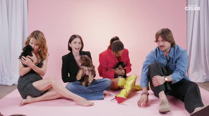 Philippine Leroy-Beaulieu, Lily Collins, Ashley Park, and Lucas Bravo sit with puppies on a pink background, smiling and interacting with the dogs