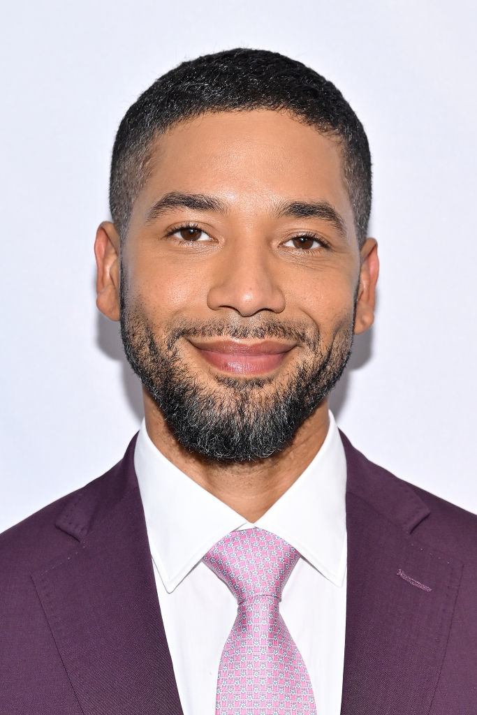 Jussie Smollett smiling at the camera, wearing a suit and tie