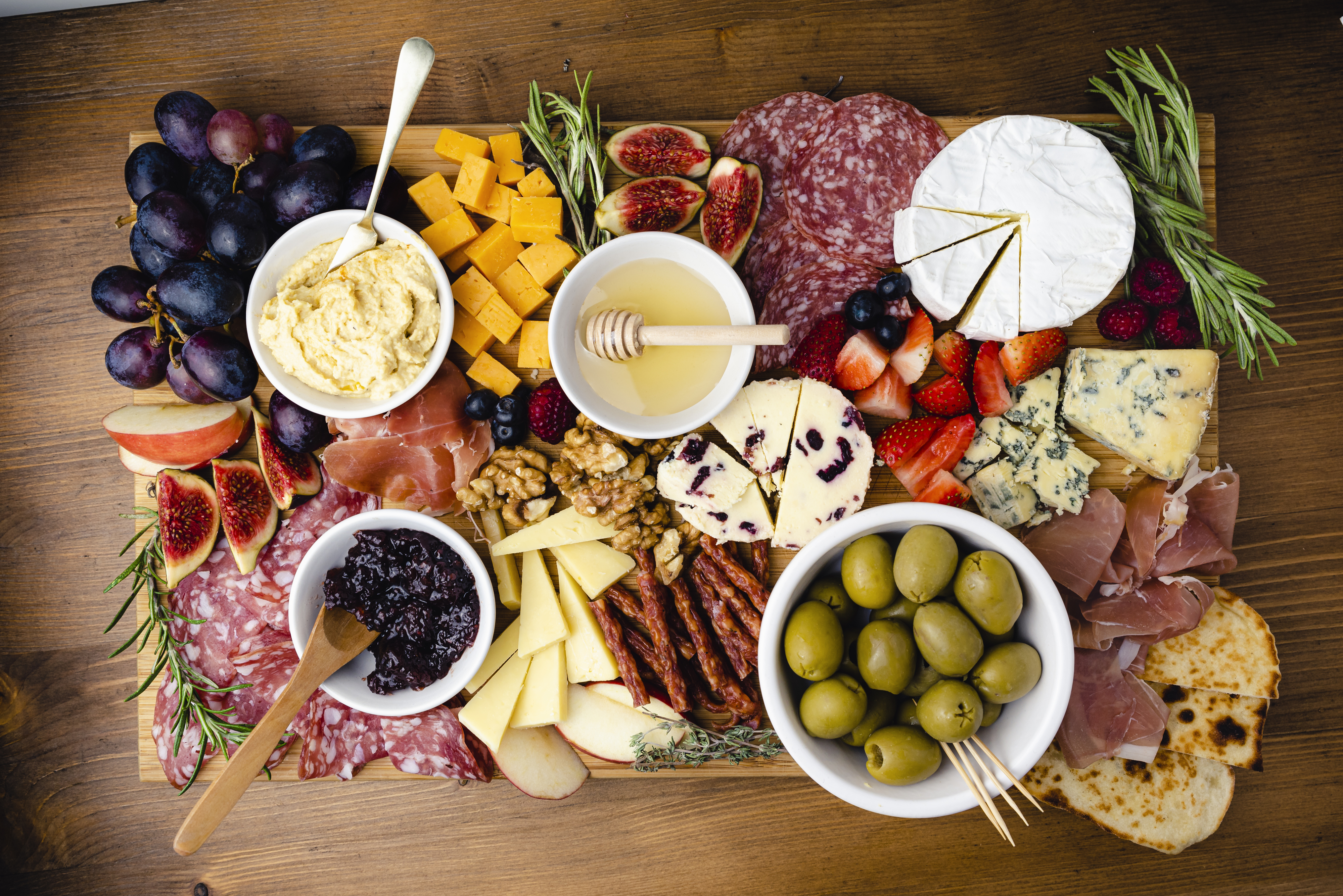 A diverse charcuterie board featuring fruits, cheeses, meats, jams, and olives, arranged on a wooden surface