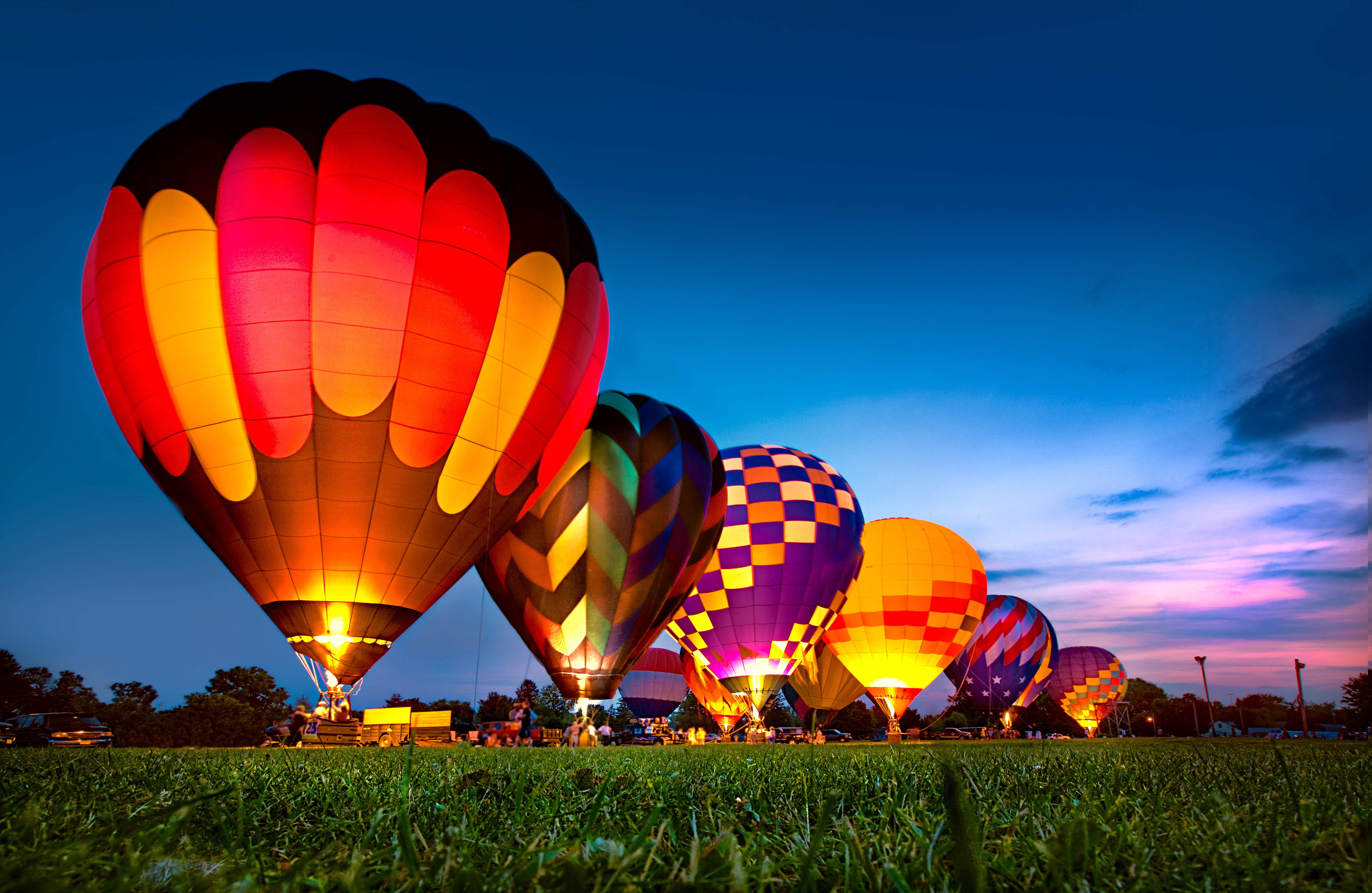 Hot air balloons of various patterns and designs preparing for takeoff at dusk in an open field