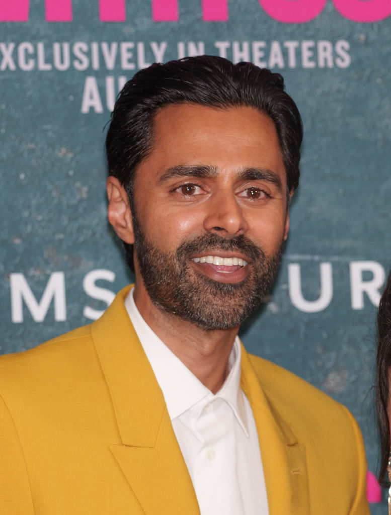 Hasan Minhaj on the red carpet, wearing a yellow blazer over a white shirt, smiling at the camera