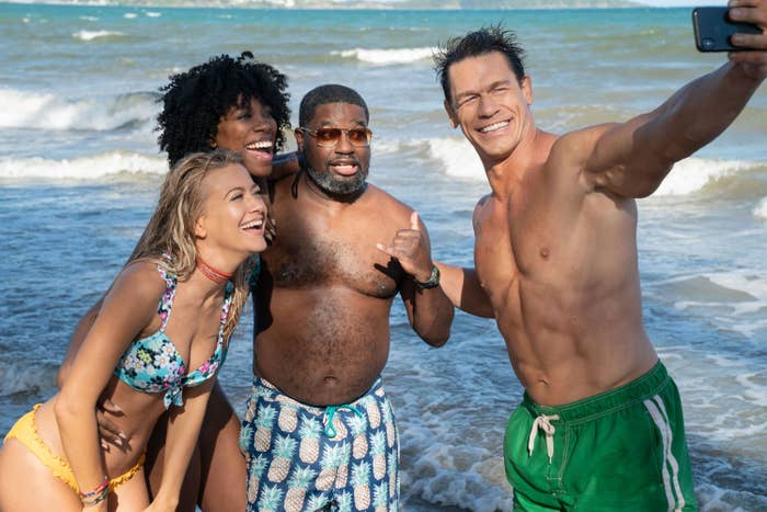 Meredith Hagner, Yvonne Orji, Lil Rel Howery, and John Cena smile for a selfie on a beach, with waves visible in the background in &quot;Vacation Friends&quot;