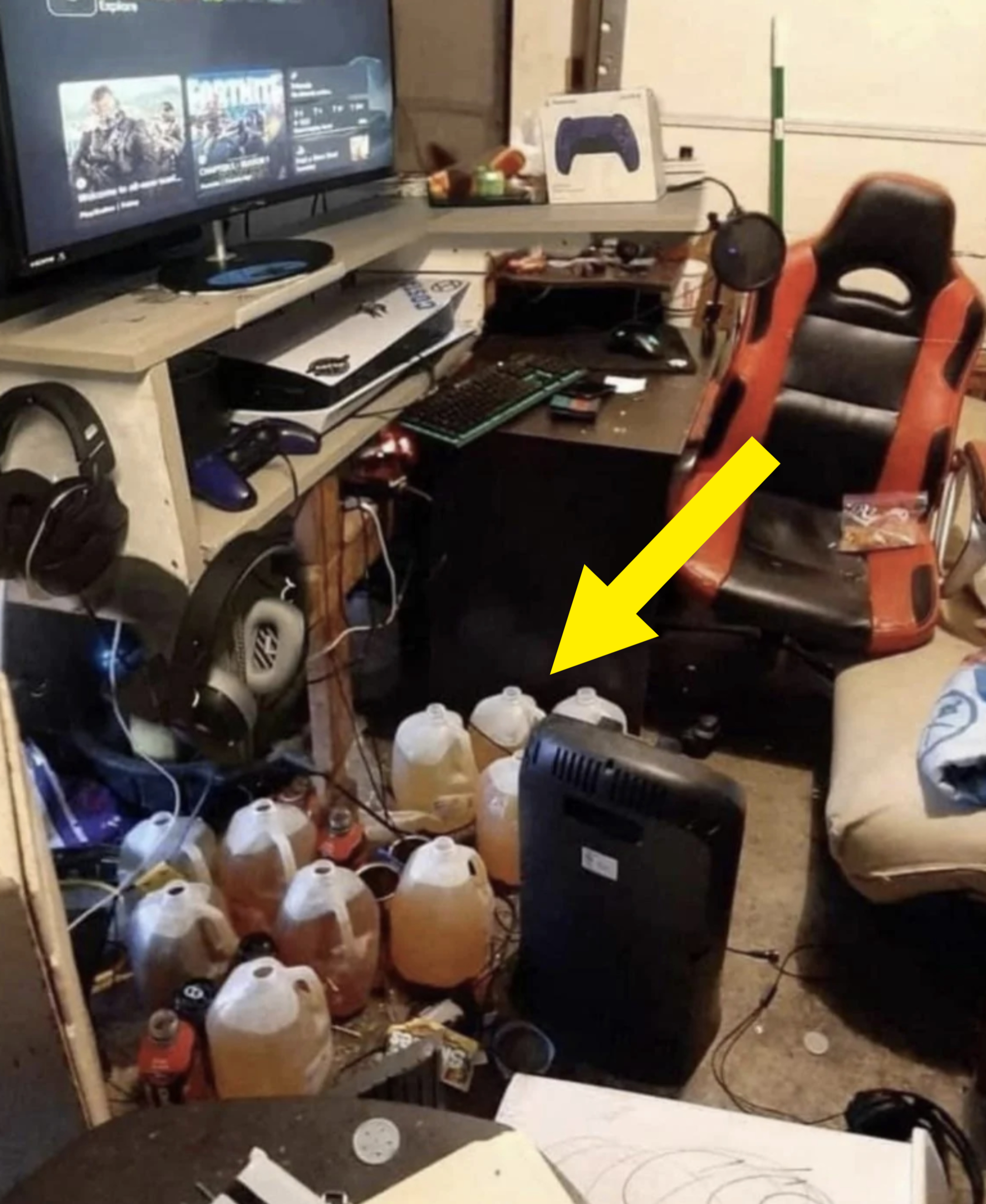 Cluttered gaming setup with multiple screens, a red and black gaming chair, and several large bottles filled with a yellow liquid on the floor